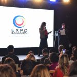 Mujer en un escenario con pantalla LED a sus espaldas con el logo Expo Inclusión