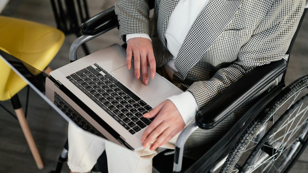 Persona sentada en una silla de ruedas con un computador portátil abierto sobre sus rodillas