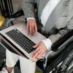 Persona sentada en una silla de ruedas con un computador portátil abierto sobre sus rodillas