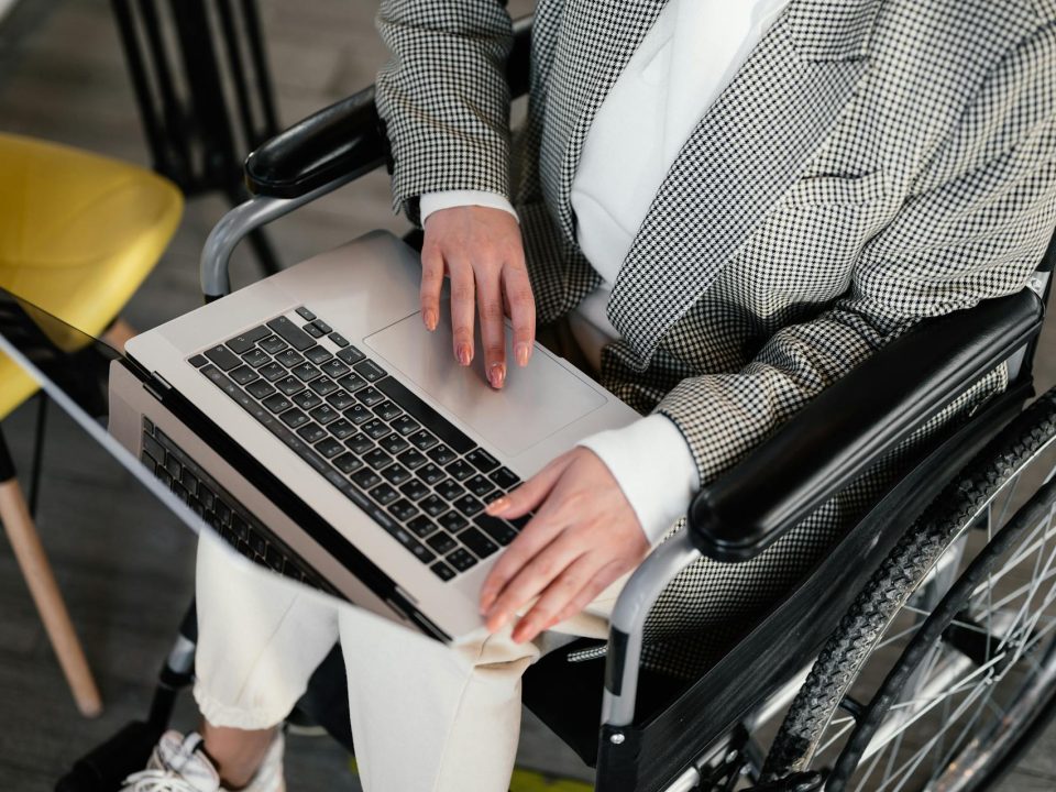 Persona sentada en una silla de ruedas con un computador portátil abierto sobre sus rodillas